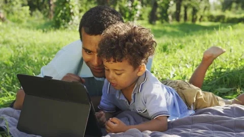 Multiethnic father and son drawing in app on tablet, have fun lying down outdoor Stock Footage 217690624