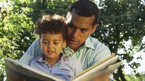 Multiethnic father and son reading big book with fairy tales and discussing plot Vídeos de archivo 217690787