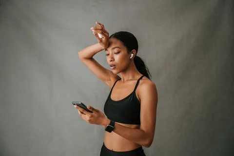 Multiethnic female perplexed on cellphone using her ear pods after gym work out Stock Photos