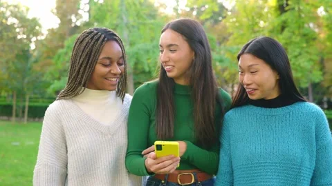 Multiethnic friends smiling while using the mobile in a park 스톡 동영상 234858611