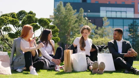 Multiethnic group of students after a good shopping take a sit down on the grass Stock-Footage 164860908