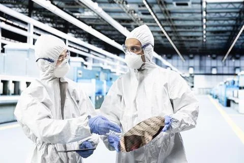 Multiethnic men processing silicon wafers in automated manufacturing plant Foto stock