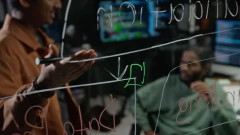 Multiethnic Programmers Discussing Code on Glass Board in Office Stockbeeldmateriaal 348370835
