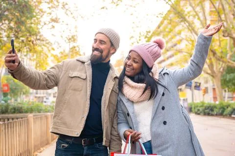 Multiethnic smiling young couple making selfie on cell phone outdoors. Stock Photos