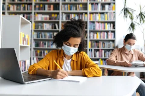 Multiethnic students study during the pandemic, sit at a tables at distance in a Stock-Fotos
