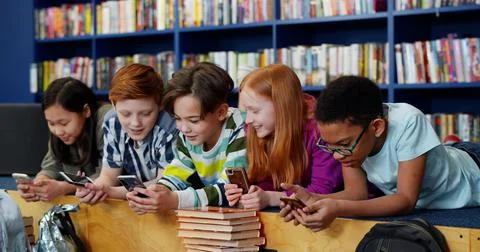 Multiethnic students using mobile phone in library at school Stock Photos
