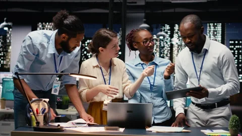 Multiethnic team collaborating in modern office workspace at night Stock Footage 334044509