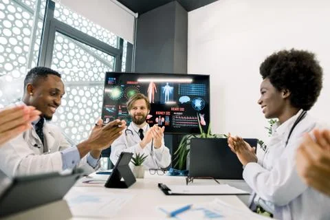 Multiethnic team of five doctors at the table, clapping their hands, applauding Stock Photos