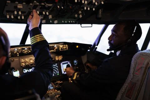 Multiethnic team of pilots using control panel in cockpit to fly airplane Foto stock