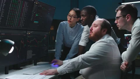 Multiethnic team of traders look at computer screens late in office Stock Footage 181144892
