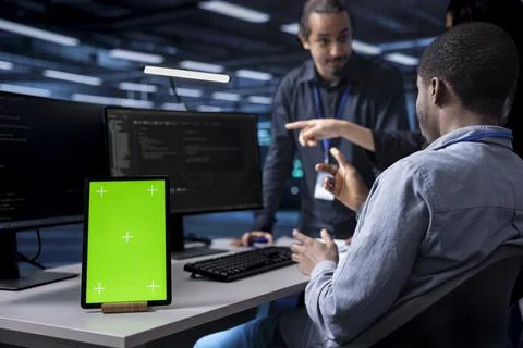Multiethnic team using green screen tablet to oversee servers 스톡 사진