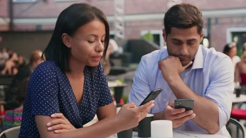 Multiethnic young couple drinking coffee sitting at cafe table outdoors using Stock Footage 158547967