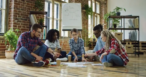 Multiethnical team of friends sitting on the floor of the co-workingspace and Stock Footage 100996978