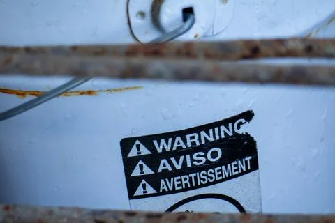 Multilingual warning label on a white bucket with rusted metal bars Stock Photos