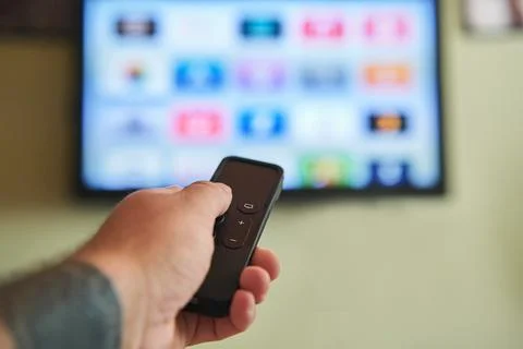 Multimedia streaming concept. Hand holding remote control. TV screen with l.. Stock Photos