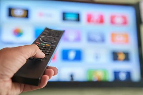 Multimedia streaming concept. Hand holding remote control. TV screen with l.. Stock Photos