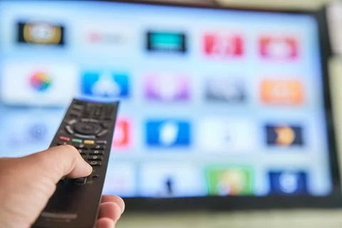 Multimedia streaming concept. Hand holding remote control. TV screen with l.. Stock Photos
