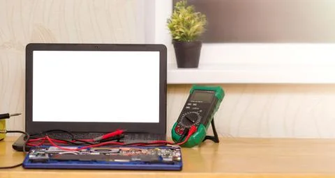 The multimeter and microcircuit lie on the table in front of an open laptop Stock Photos