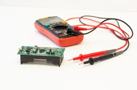 A multimeter with test probes and a circuit board lie on a white background. Stock Photos