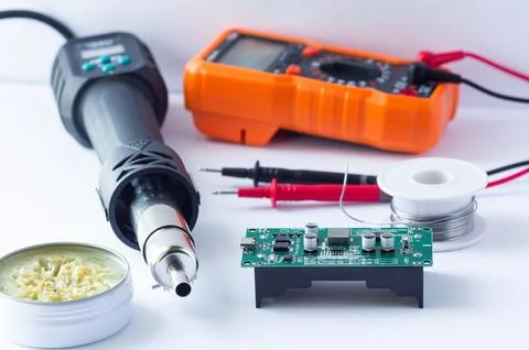 A multimeter with test probes, a hot air gun, and tools lie on a white backgr Stock Photos