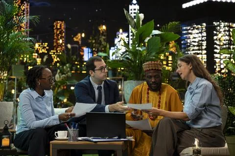 Multinational coworkers reading documents on rooftop terrace at night Fotos de archivo
