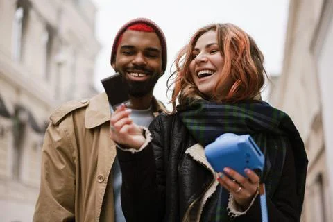 Multinational joyful couple laughing while looking on instant photo Stock Photos