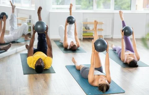 Multinational students repeats movements of coach, lying on mat with hands with Stock Photos