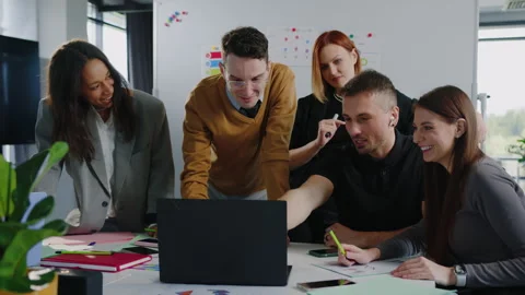 Multinational team stands in front of a laptop and discusses about project Stock Footage 257420241