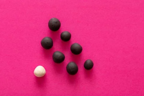 Multiple black balls and single white one on pink background. Concepts of rac Stock Photos