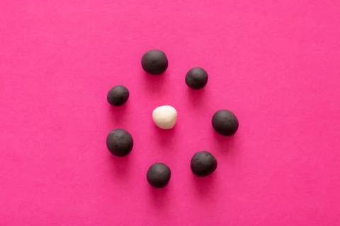 Multiple black balls surrounding a single white one on pink vibrant backgroun Stock Photos