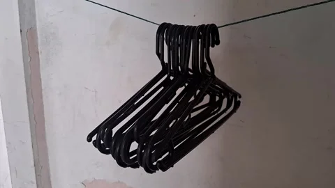 Multiple black plastic clothes hangers hanging on string motion video footage Stock Footage 339349220