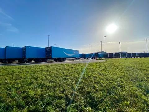 Multiple blue Amazon prime trailers are parked within a waiting are close to the Stock Photos