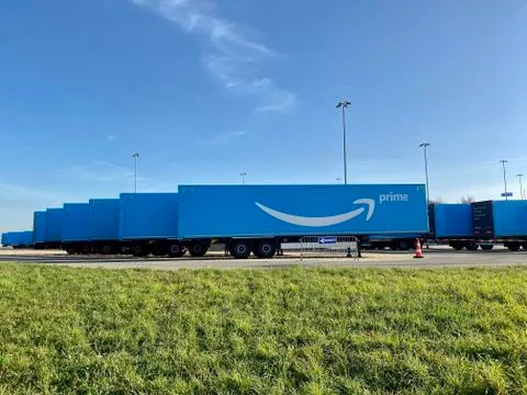 Multiple blue Amazon prime trailers are parked within a waiting are close to the Stock Photos