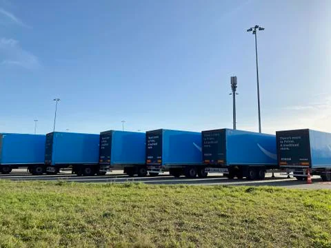 Multiple blue Amazon prime trailers are parked within a waiting are close to the Stock Photos