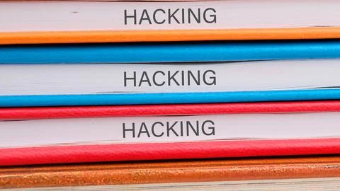 Multiple books focused on the topic of hacking are neatly arranged on a woode Stock Photos