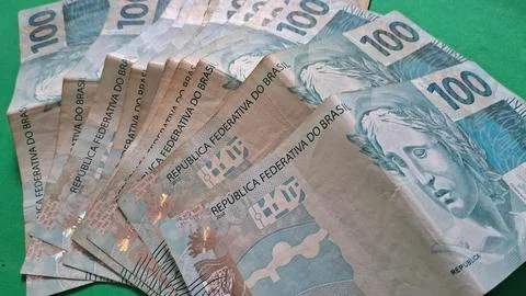 Multiple Brazilian one hundred real banknotes spread out on green surface Stock Photos
