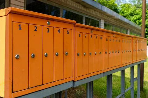 Multiple bright orange mailboxes are arranged neatly outside a building surro Stock Photos