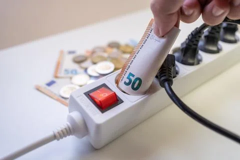 Multiple cables plugged into a power strip and money representing the high cost Stock Photos
