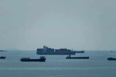 Multiple Cargo Ships Navigate The Open Ocean During An Overcast Day Wide Shot Stock Photos