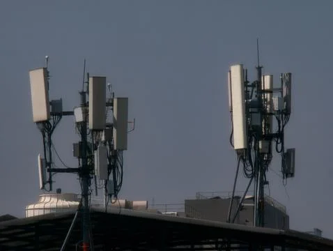 Multiple Cell Phone Tower Antennas on Building Rooftop Against Blue Sky Foto stock