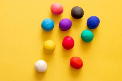 Multiple colored plasticine balls on a yellow background. All scatered random Stock Photos