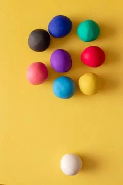 Multiple colored plasticine balls on a yellow background, one white not a par Stock Photos