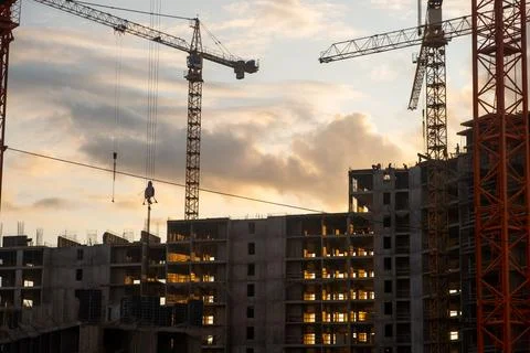Multiple cranes work efficiently at a construction site as the sun sets, il.. Stock Photos