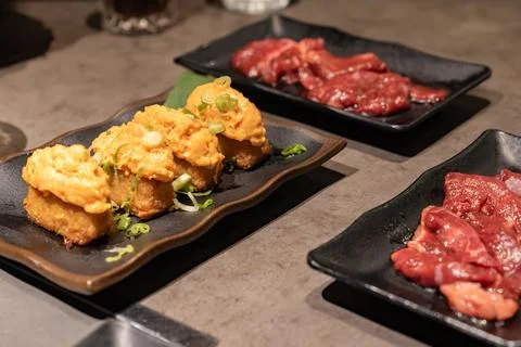 Multiple dishes served on dark plates including spicy salmon and raw meat. .. Stock Photos