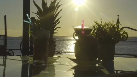 Multiple drinks on a table with sun setting into the sea behind Stock Footage 140056134