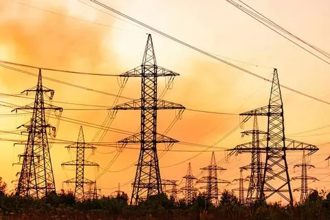Multiple electrical towers standing in a field at sunset Stock Photos