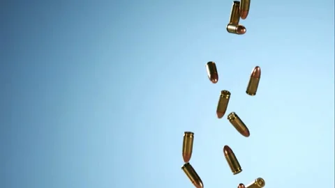 Multiple gold colored bullets fall against a plain blue background Stock Footage 326628012