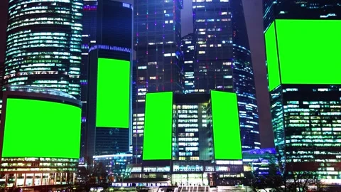 Multiple green screen billboards are mounted on modern skyscrapers at night Video stock 288308082
