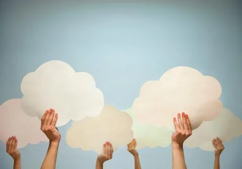Multiple hands holding cut out paper clouds against a blue background, stud.. Stock Photos