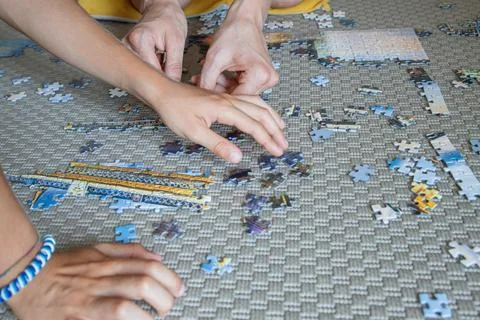 Multiple hands work together on a large jigsaw puzzle on a carpeted floor Stock Photos